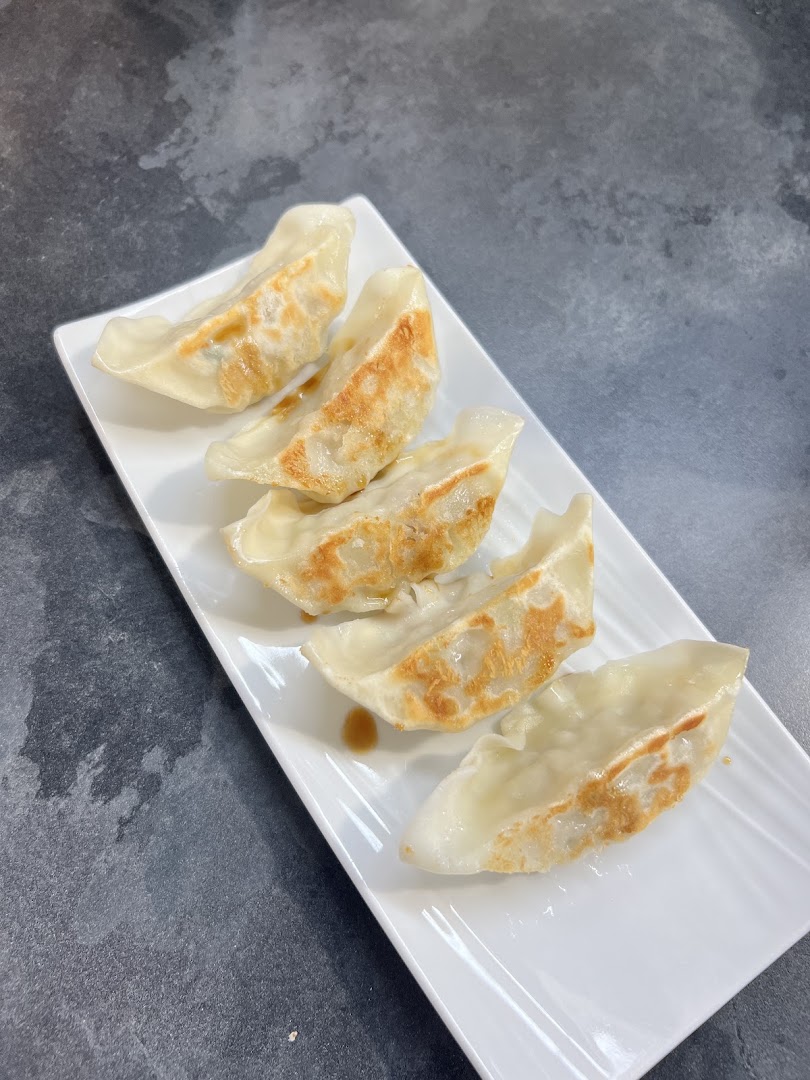 Cinq raviolis japonais dorés sur une assiette blanche